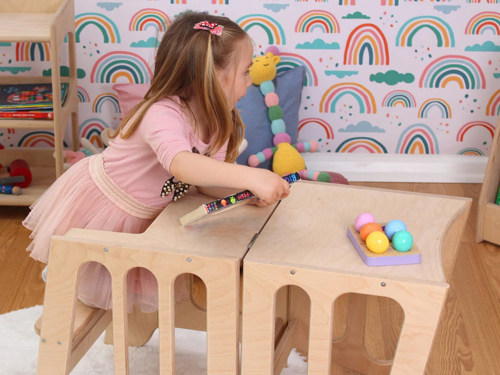 a little girl sitting at a wooden table playing with toys