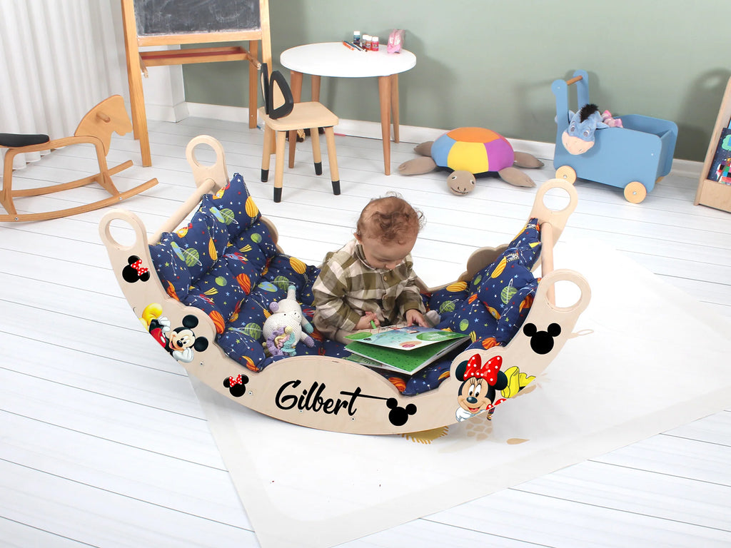 a baby sitting in a mickey mouse chair reading a book